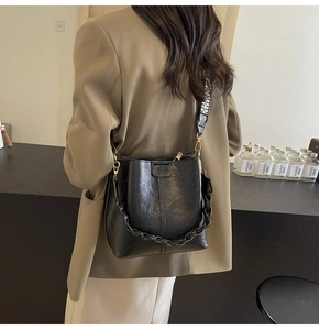 Close-up of black bucket bag with braided handle and geometric wide fabric strap