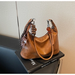 Detailed view of brown leather handbag with cat and chocolate charms on a leather sofa