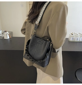Close-up of black matte bucket bag with woven wide strap and thick chain handle details
