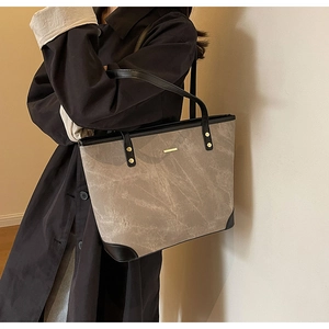 Detail of stone textured leather tote bag featuring gold studs and black reinforced corners