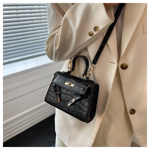 Detail view of black crocodile pattern bag with elegant gold hardware on a chic model