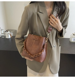 Detail of dark brown leather bucket bag with woven patterns and geometric shoulder strap