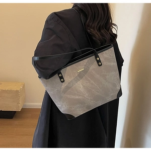 Minimalist grey tote bag with vintage texture and black leather straps on a female model