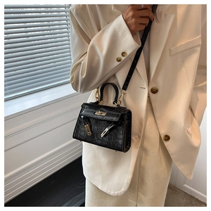 Detail of black crocodile-embossed mini handbag with gold-tone hardware on white suit