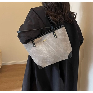 Detail of a large grey vintage tote bag with black trim worn by a model in a minimalist room