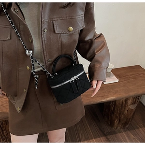 Detail of black quilted chain vanity bag with rhombic pattern and metal handle