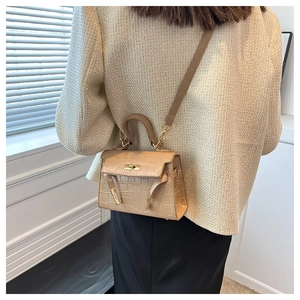 Detail view of mini beige crocodile pattern leather bag with metallic twist lock and strap