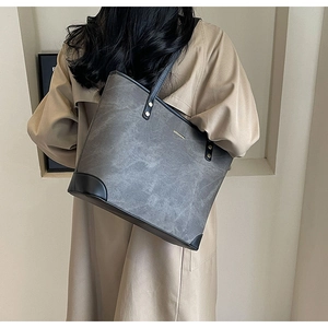 Detail of a large grey vintage tote bag with black trim and rivets on a beige trench coat