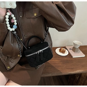 Detail of black quilted mini bag with double zippers and elegant pearl charm accessory