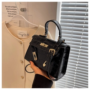 Detail of black crocodile pattern handbag with gold twist lock on white coat background