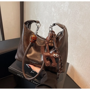 Detail of dark brown leather shoulder bag featuring a cat charm and amber bead decor