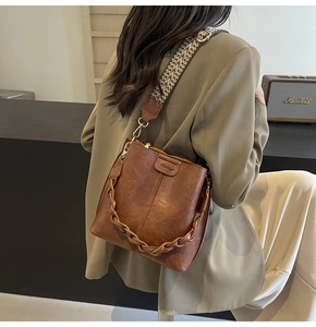 Macro shot of brown faux leather bucket bag detailing wide knit strap and embossed logo