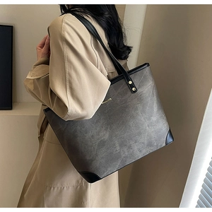 Detailed view of large grey tote bag with black handles and rivets on model