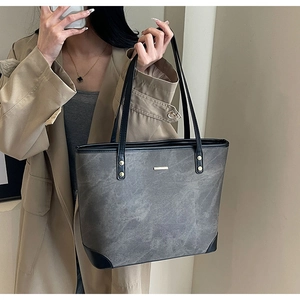 Detailed view of grey tote bag with black trim and long handles on a model in a trench coat