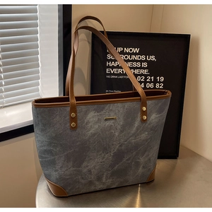 Detail of stone textured tote bag featuring brown leather trim and golden rivets