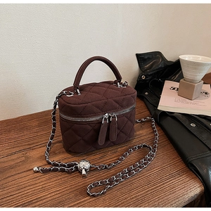 Detail of dark brown quilted crossbody bucket bag with silver skull charm and chain