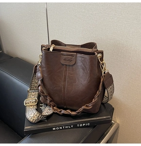 Macro detail of dark brown leather bucket bag with ethnic textured wide strap and braided handle