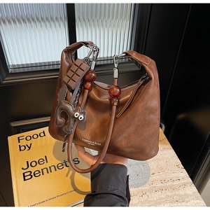Detail of vintage brown leather bag with cat charm and chocolate pendant on marble