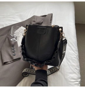 Detail of black bucket bag with textured leather, wide patterned strap and chain handle