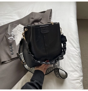 Detail view of black bucket bag with bohemian wide strap and woven handle on fabric background