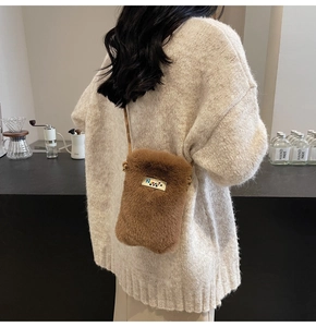 Détail d'un petit sac à bandoulière en peluche marron avec logo en métal et fine lanière