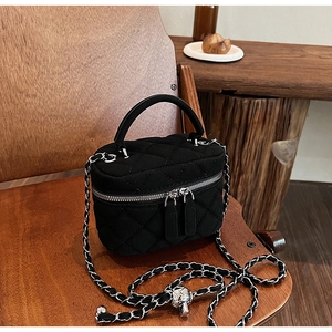 Close-up of black quilted vanity bag with metal chain strap and top handle detail