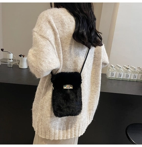 Détail d'un mini sac bandoulière en peluche noire avec étiquette sur un pull