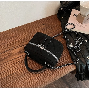 Detail of black quilted box-shaped handbag with silver chain strap and dual zipper closure