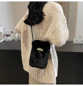 Petit sac bandoulière noir en peluche avec écusson coloré sur fond de pull en maille douce