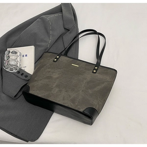 Detail of taupe tote bag with black leather trim and elegant gold metal hardware bar