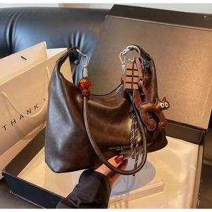 Detail of a brown leather hobo bag with amber bead strap and cute cat charm in a gift box