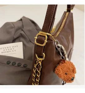 Detail of dark brown leather handbag with gold hardware and plush teddy charm accessory