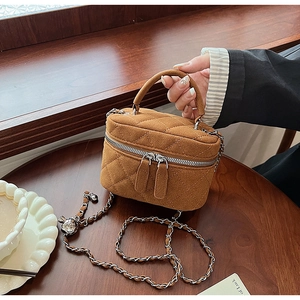 Detail of a brown suede vanity bag with quilted stitching and chain strap