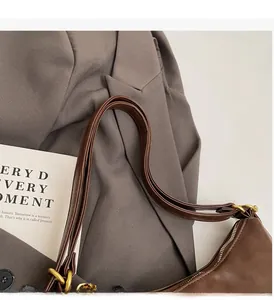 Detail view of dark brown leather shoulder bag with gold metal buckle and smooth zipper