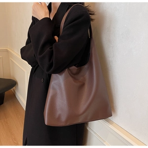 Brown lychee leather tote bag shown on a model wearing a black coat in a chic indoor setting
