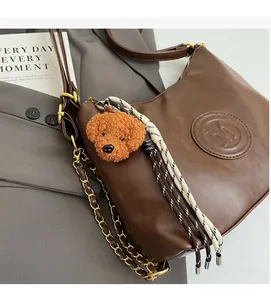 Detail of caramel brown leather tote bag with embossed M logo and plush dog charm