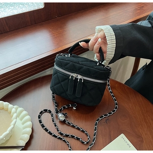 Macro shot of black quilted mini bucket bag with silver chain strap on wooden table