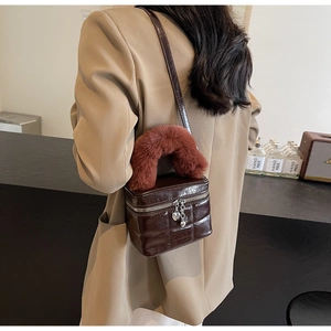Detail der dunkelbraunen Box-Tasche mit rotem Plüschgriff und Herz-Anhänger am Reißverschluss