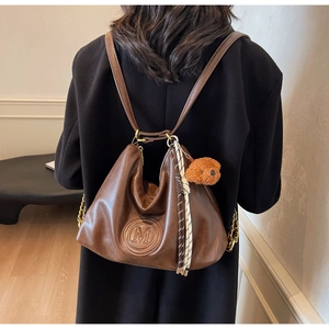 Detail view of brown faux leather backpack featuring embossed M logo and bear charm
