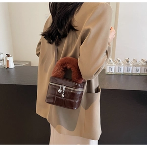 Detail einer braunen gesteppten Box-Tasche mit flauschigem Plüschgriff und Herzanhänger