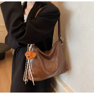 Detailed view of vintage brown leather bag with embossed M logo and teddy bear charm