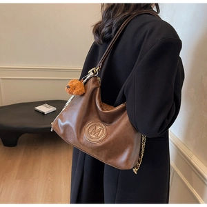 Detail of vintage brown tote bag with M logo, chain strap and plush bear charm on model