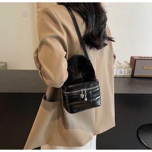 Detail einer schwarzen gesteppten Box-Tasche mit Plüschgriff und Herzanhänger am Model