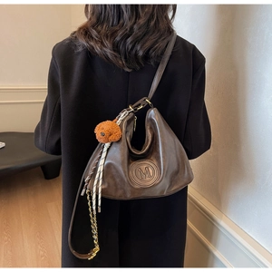 Detail of a brown leather hobo bag with M logo embossing and a cute bear charm
