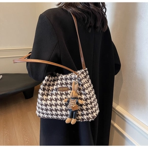 Detail of houndstooth shoulder bag with a brown leather logo and a plush rabbit charm