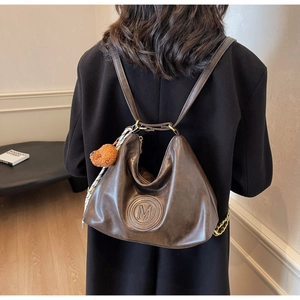 Detail of dark brown leather tote backpack with embossed M logo and bear charm