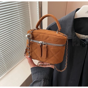 Detail of brown quilted velvet handbag featuring silver chain strap and metal ball charm