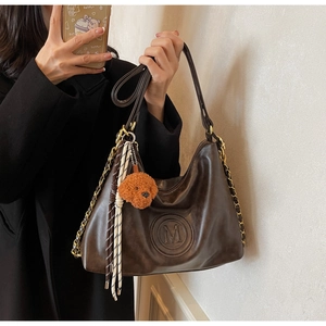 Detail of dark brown faux leather hobo bag with gold chain and plush dog pendant