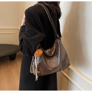 Detail of dark brown leather tote with embossed M logo and cute plush bear charm
