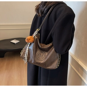 Detail of dark brown leather shoulder bag with embossed M logo and bear charm